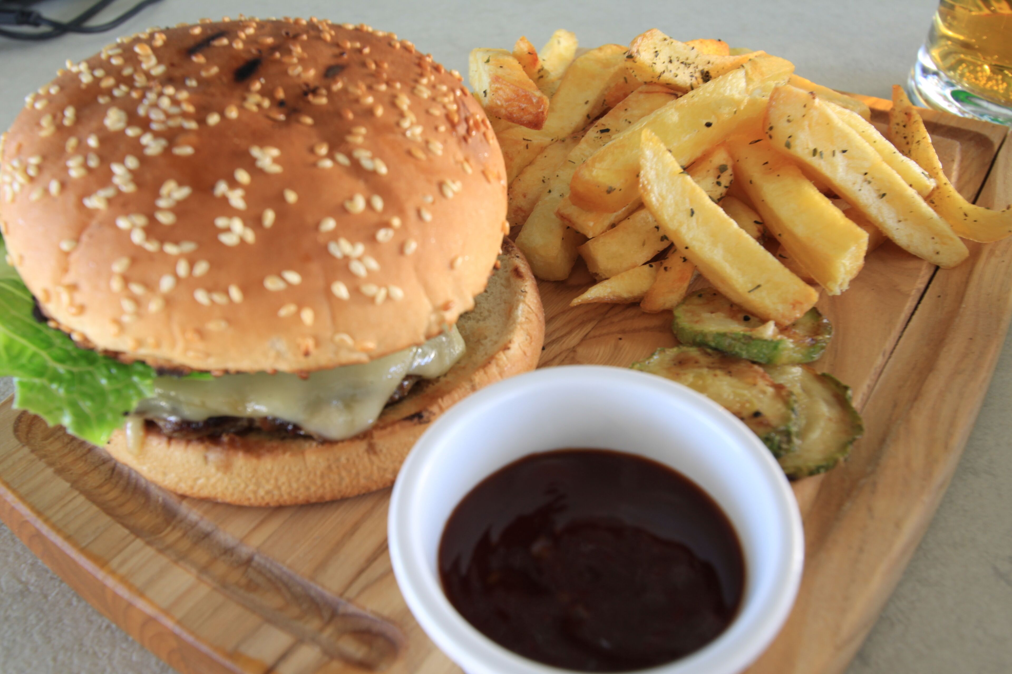 A meal consisting of a hamburger, French fries, and a small bowl of sauce on a wooden tray.