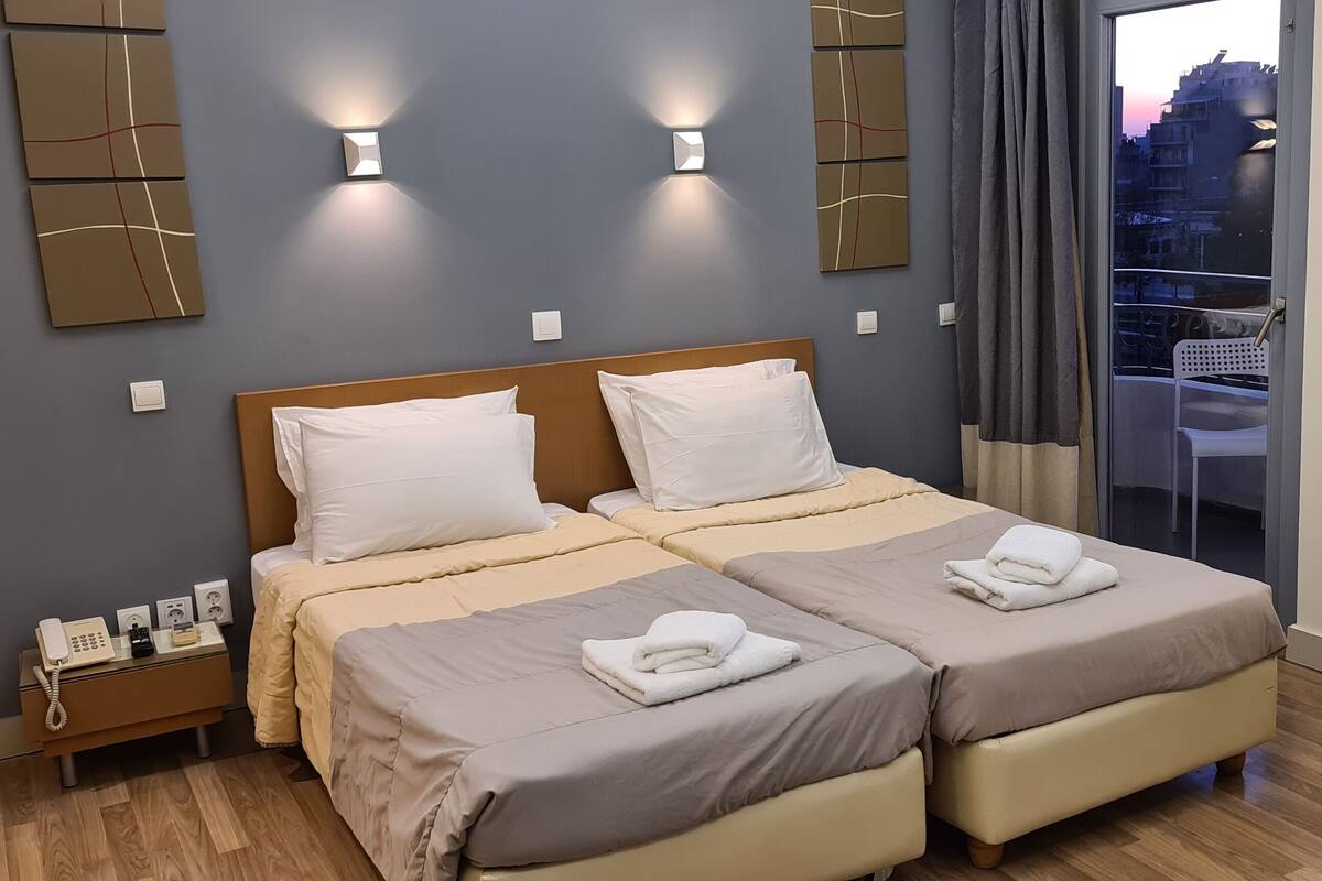 Ein Hotelzimmer mit zwei Betten, einem Nachttisch mit Telefon und Blick auf die Stadt.