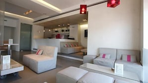A modern hotel lobby with a minimalist design, featuring a seating area with sofas and a coffee table, a reception desk, and a visible kitchen area in the background. - Ariston (Athens)