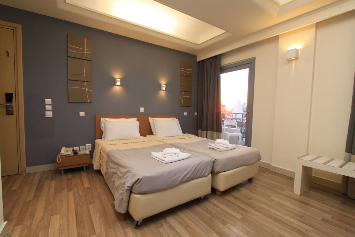 Ein Hotelzimmer mit zwei Betten, Holzboden, Schreibtisch mit Telefon und einer Bank.