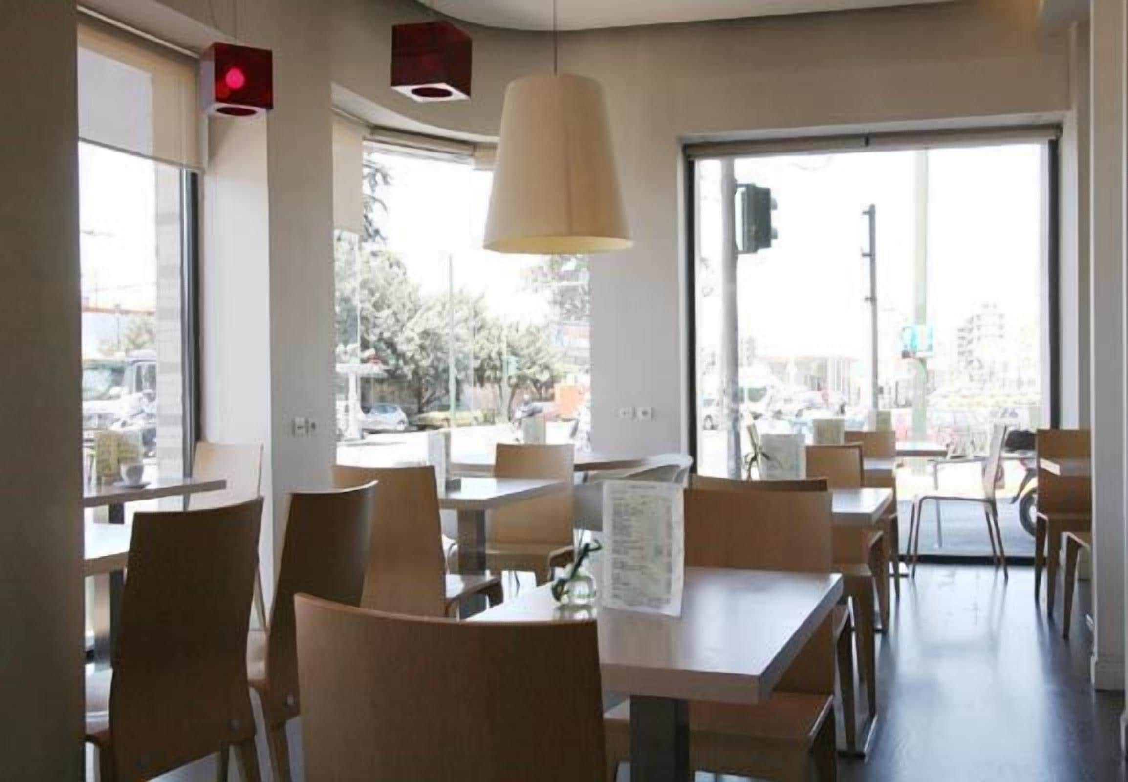 Interior de un restaurante con mesas, sillas, ventanas amplias y una lámpara colgante.