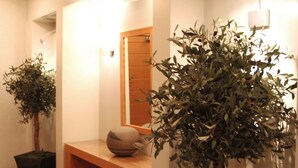 A hallway with a wooden bench, two potted plants, a mirror, and recessed ceiling lights. - Pines Hotel (Kifisia)