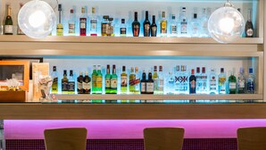 A bar with shelves of liquor bottles and two large spherical light fixtures. - Pines Hotel (Kifisia)