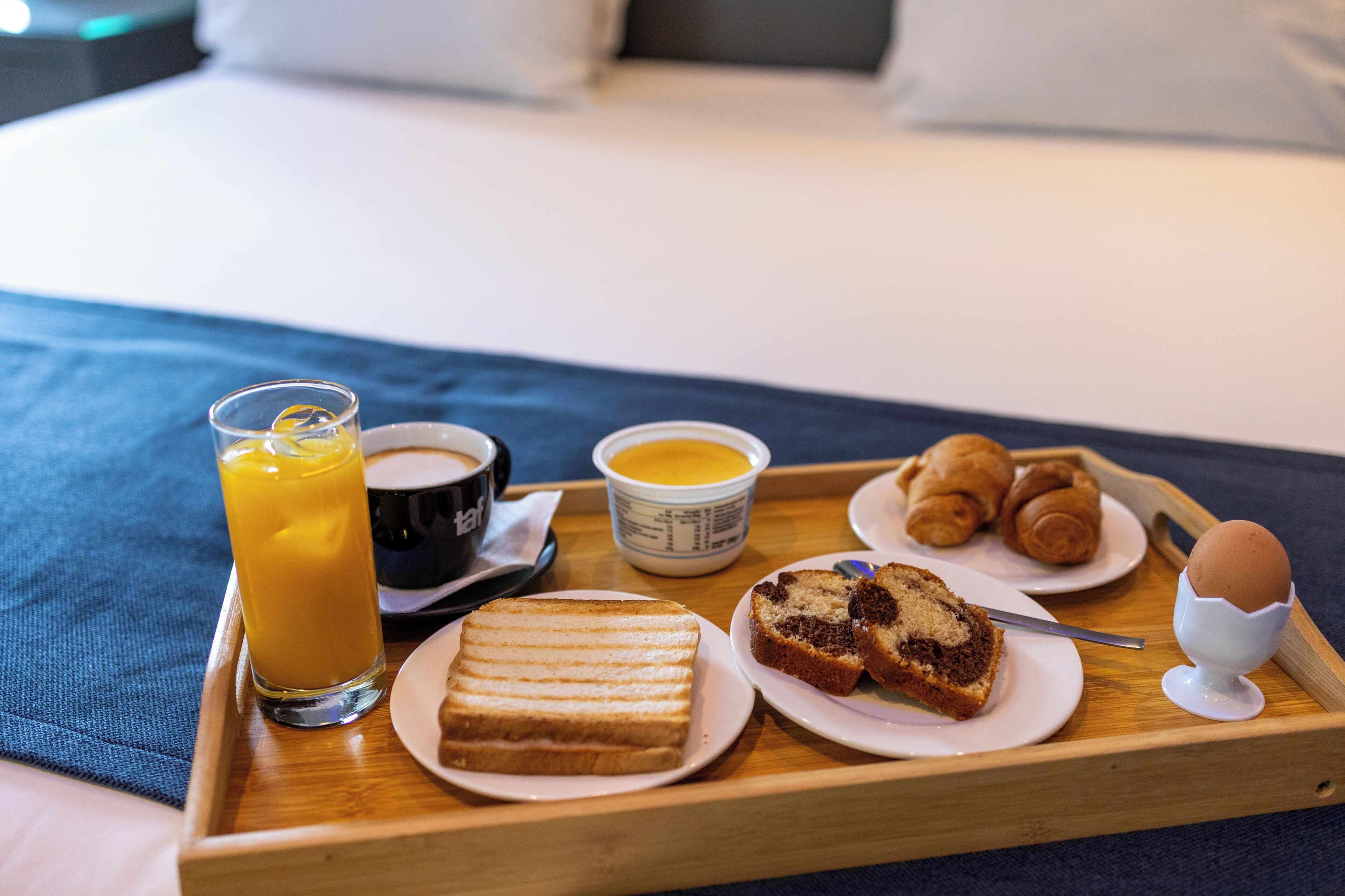 A breakfast tray with a glass of orange juice, a cup of coffee, a bowl of soup, a slice of bread, a muffin, and an egg on a wooden tray.