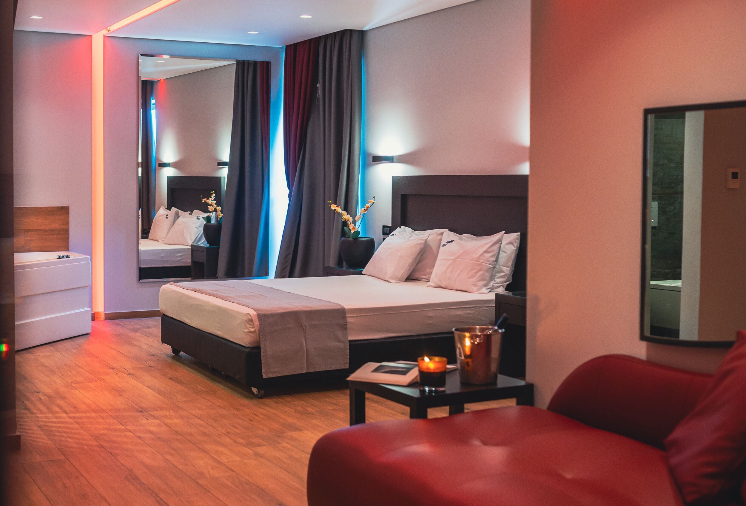 Una habitación de hotel moderna con cama, mesita de noche, sillón de cuero rojo y un espejo grande.