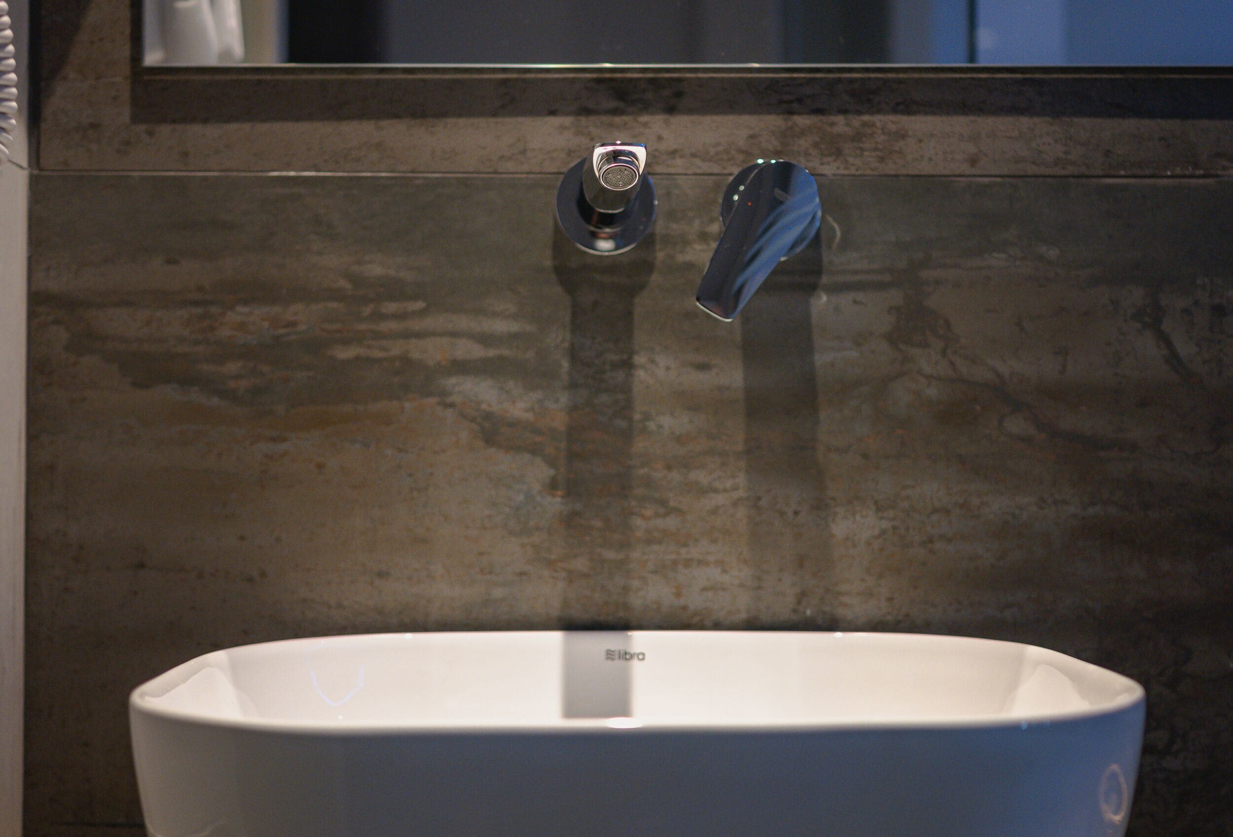 A bathroom with a white sink, a mirror above it, and a wall with a textured finish.