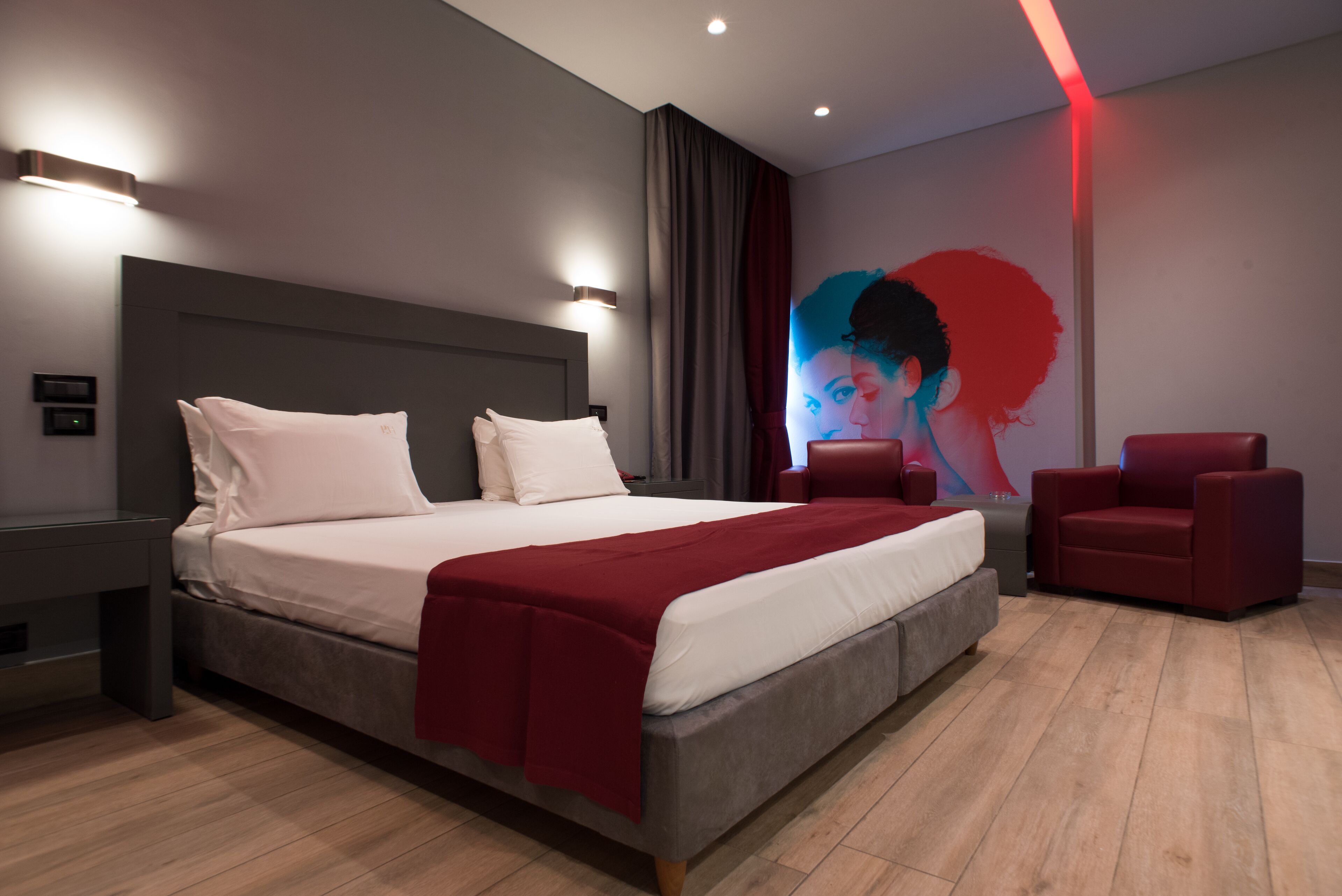 A modern bedroom with a large bed, a red chair, and a wall mural.