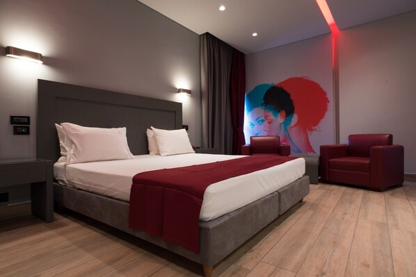 A modern bedroom with a large bed, a red chair, and a wall mural.