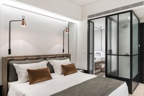 A modern hotel room with a large bed, two bedside lamps, a wardrobe with frosted glass doors, and a bathroom visible through the wardrobe. - Niki Athens Hotel (Athens)
