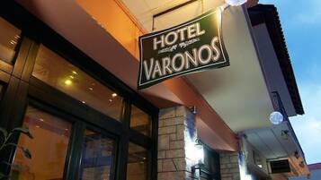 Ein Schild des Hotels 'Hotel Varonos' mit einer Stein-Fassade und großen Fenstern.