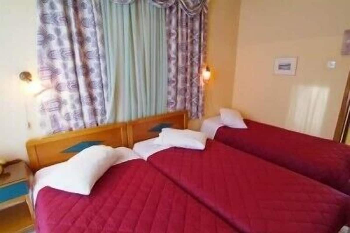 A double bed with red bedding, a wooden headboard, and a nightstand with a lamp.