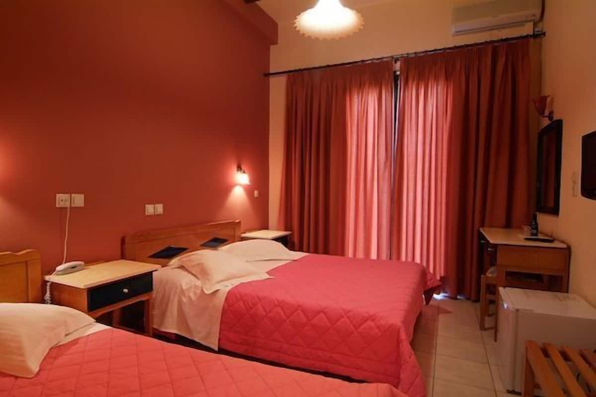 A hotel room with two beds, a desk, a chair, a small table, and a TV.