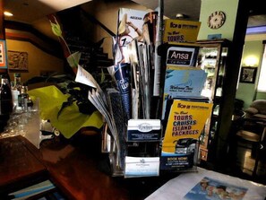 A bar area with a counter displaying various promotional materials and a clock on the wall. - Pergamos (Athens)