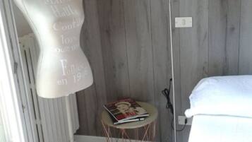 Una habitación con un maniquí en una esquina, una mesita redonda con una revista, una lámpara de pie y una cama.