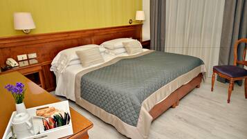 Een hotelkamer met een bed, nachtkastje, lamp, stoel en een dienblad met ontbijtartikelen.