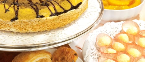 A variety of baked goods including a cake with chocolate drizzle, a bowl of sliced peaches, and a plate of round pastries.