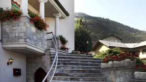 Una escalera de piedra que conduce a un edificio con fachada blanca y un balcón adornado con flores rojas.
