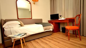 A hotel room with a bed, a desk with a computer, a chair, a mirror, and a lamp.
