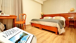 Habitación de hotel con cama de madera, un escritorio y una silla. Hay un libro sobre el escritorio y una lámpara en la mesita de noche.