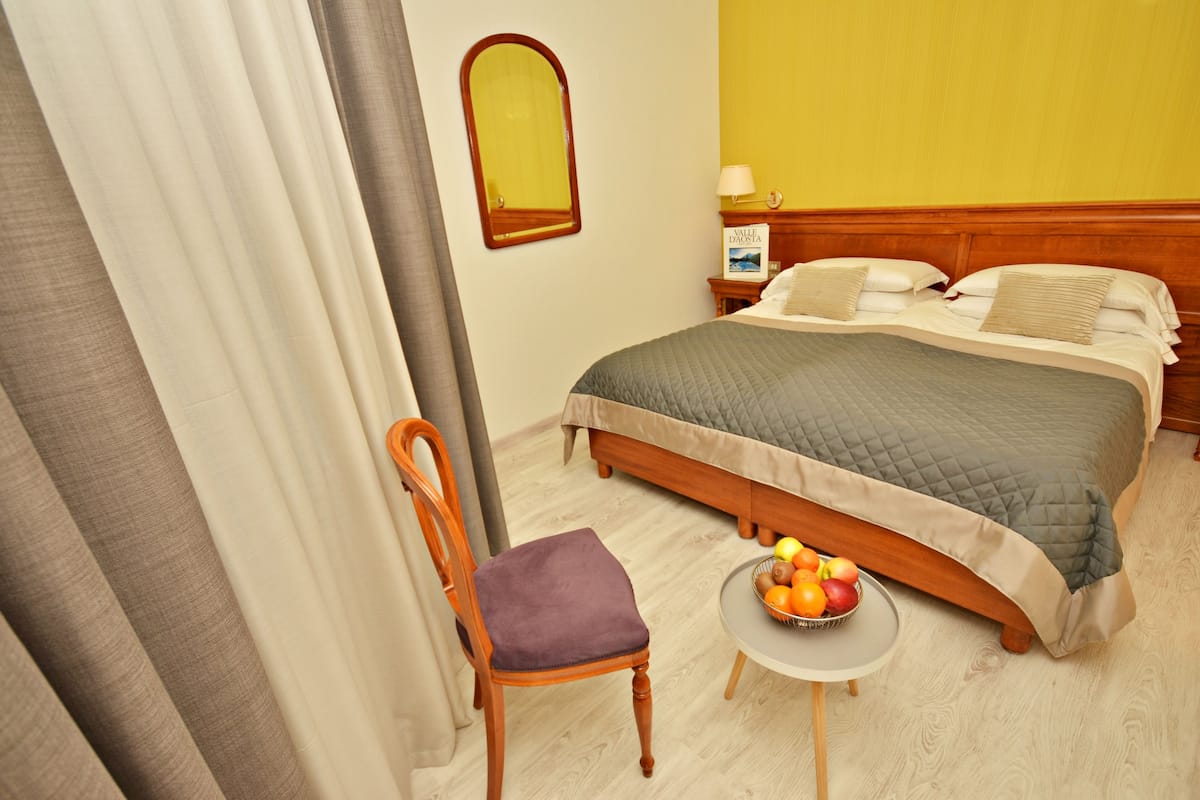 Habitación de hotel con cama, una silla, una mesita con fruta y un espejo en la pared.