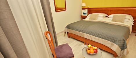 Habitación de hotel con cama, una silla, una mesita con fruta y un espejo en la pared.