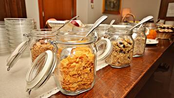 Una mesa de buffet con diferentes alimentos en recipientes de vidrio, como cereales y granola.
