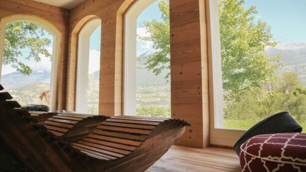 Una habitación con paredes de madera y grandes ventanas arqueadas que ofrecen vistas a la vegetación y montañas.