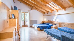 A room with a wooden ceiling, a bed with a blue bedspread, a desk with a chair, and a window with curtains.