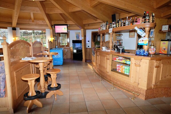 Un interior de madera con zona de bar, taburetes de madera y un televisor.
