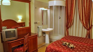 Une chambre d’hôtel comprenant un lit, un bureau avec une télévision, un lavabo et une douche.