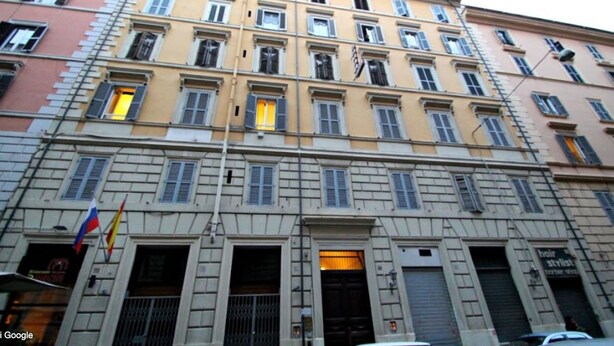 Un immeuble à plusieurs étages, de style architectural classique, avec une entrée centrale dotée d’une porte sombre et un petit balcon situé juste au-dessus.