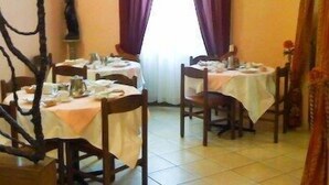 Un coin repas avec deux tables, chacune recouverte d’une nappe blanche. Des chaises sont disposées autour des tables, et une fenêtre avec des rideaux violets est visible au fond.