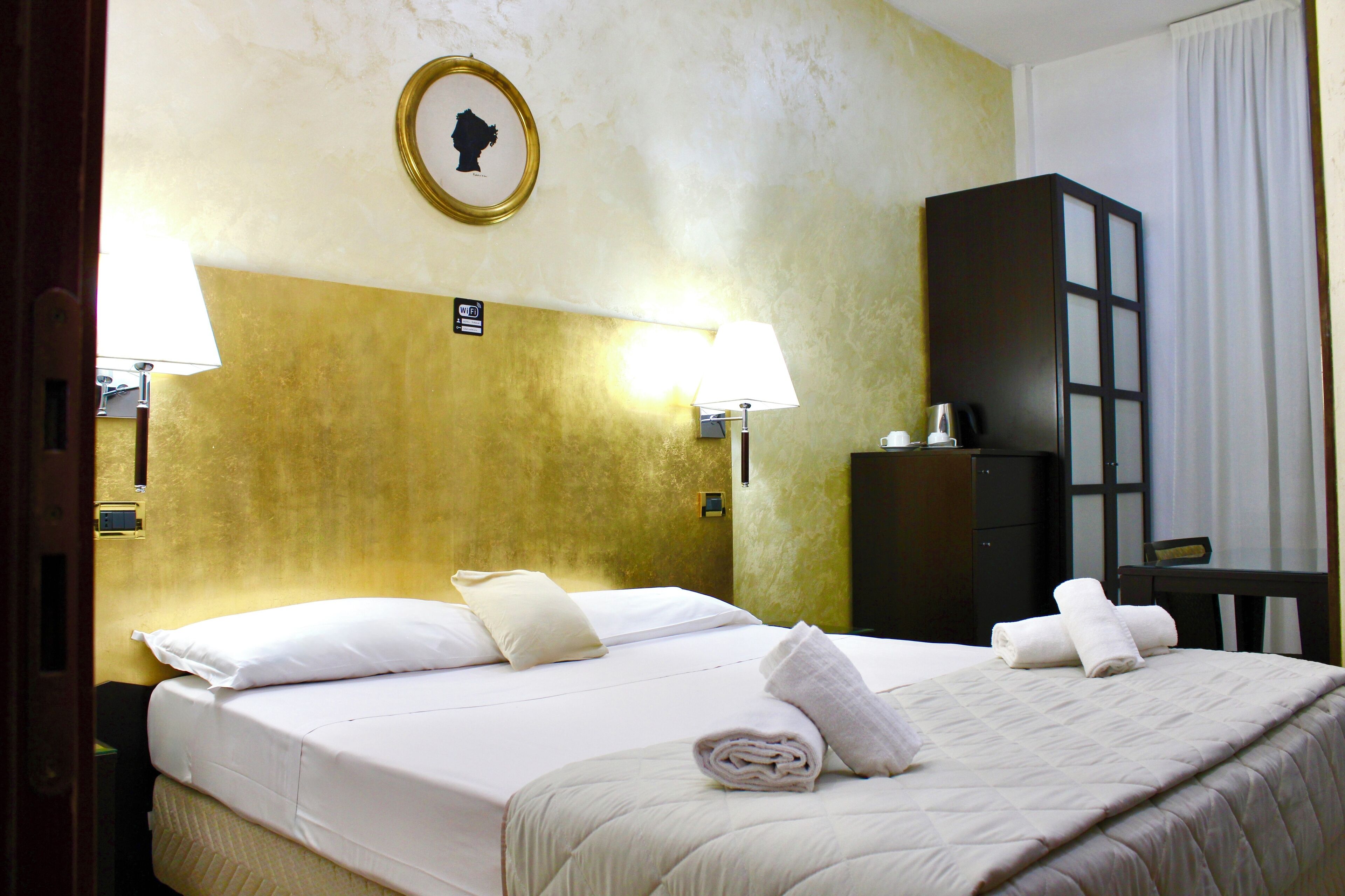Une chambre d’hôtel avec un lit, deux lampes de chevet, une table de chevet, une commode et un tableau encadré au mur.