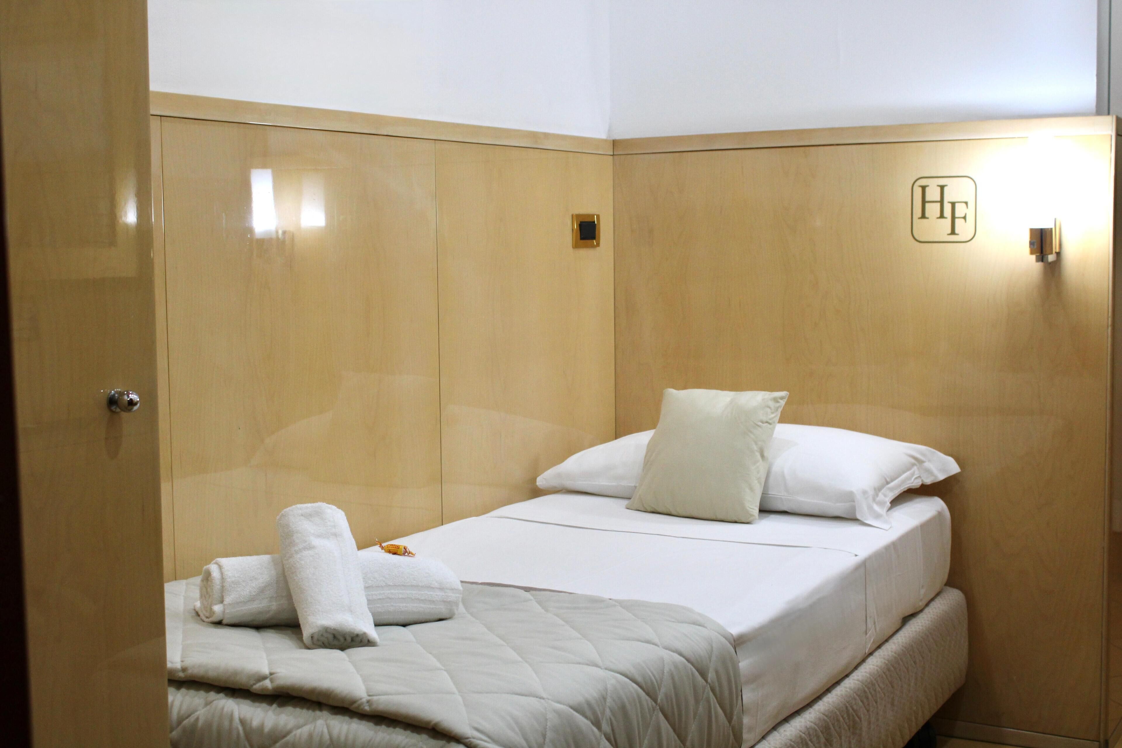A hotel room with a bed, a bedside table, a nightstand, and a wardrobe.