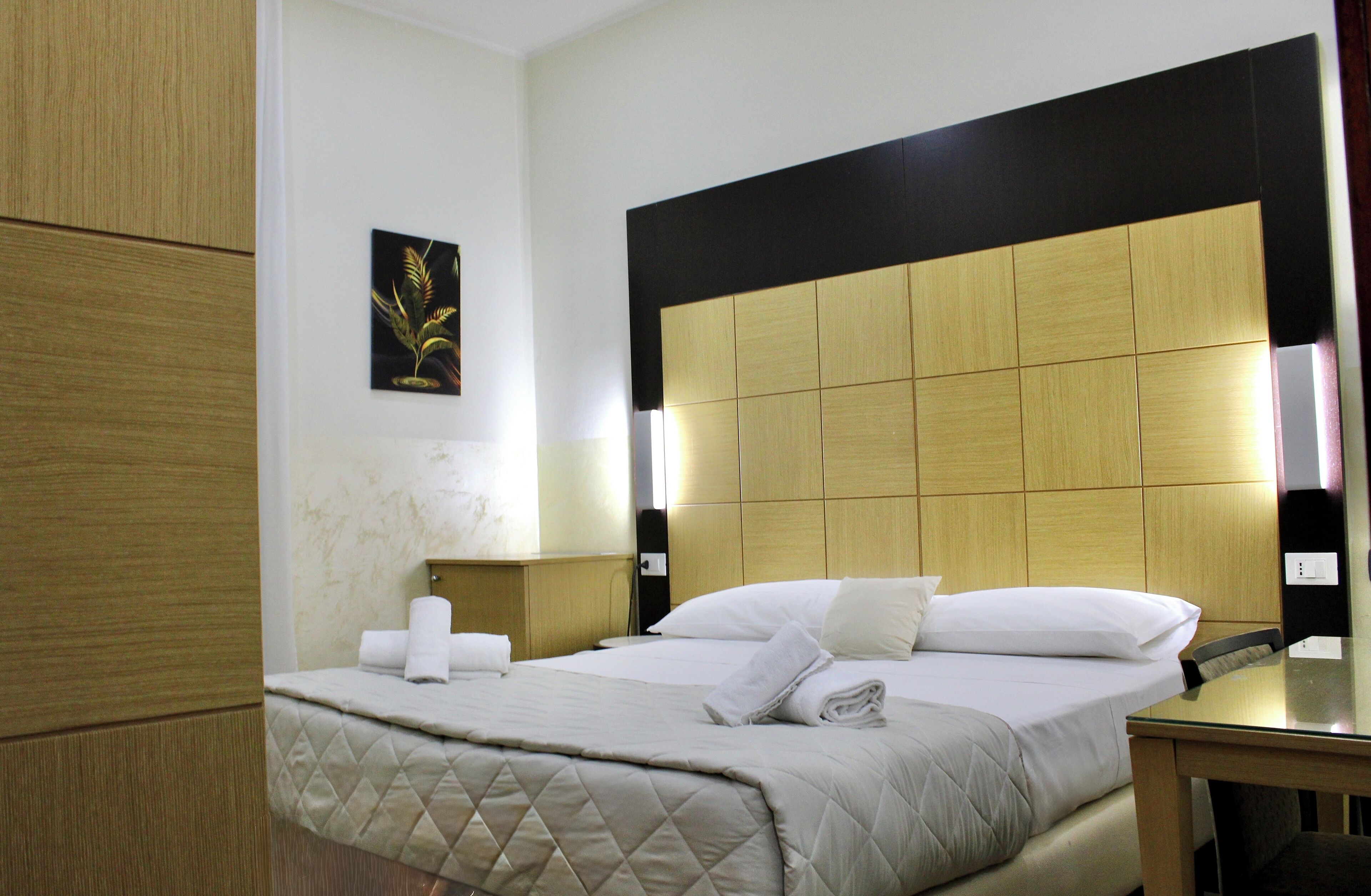 A hotel room with a large bed, a wooden headboard, a bedside table, and a wall-mounted picture.