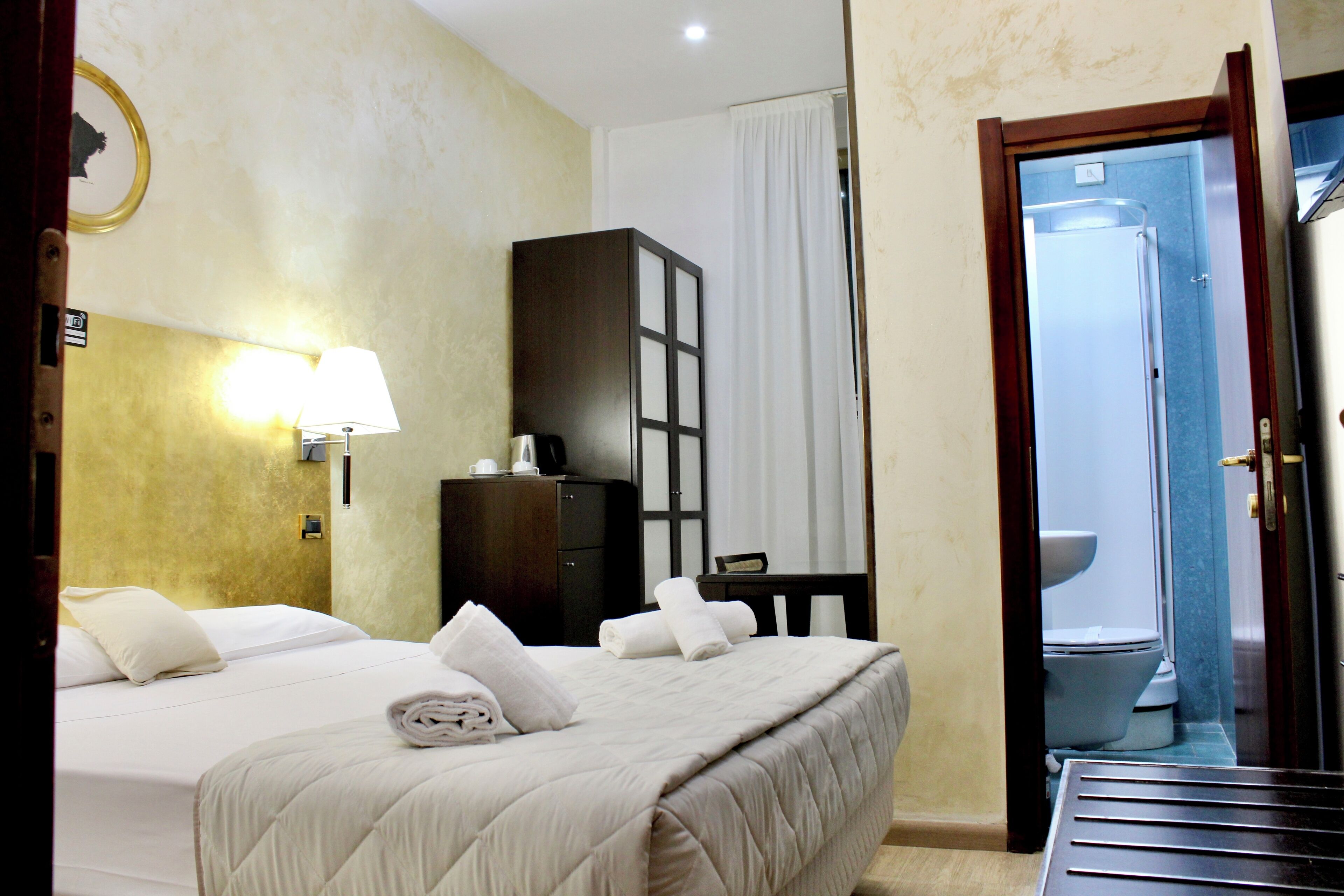 Ein Hotelzimmer mit Bett, Schreibtisch, Kleiderschrank und einem durchgegangenen Tür sichtbaren Badezimmer.
