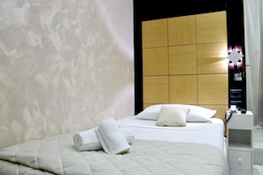 A modern hotel room with a neatly made bed, a wooden headboard, and a bedside table with a phone and a Wi-Fi symbol.