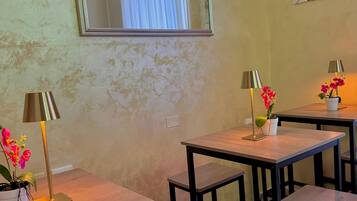 Una habitación con un espejo grande, dos mesitas con lámparas y flores, y un adorno en la pared.