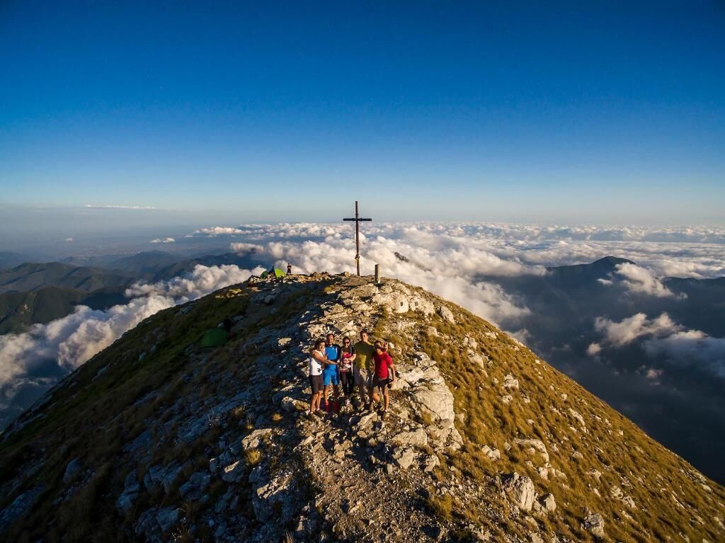 A group of people on a mountain peak with a cross, surrounded by clouds.