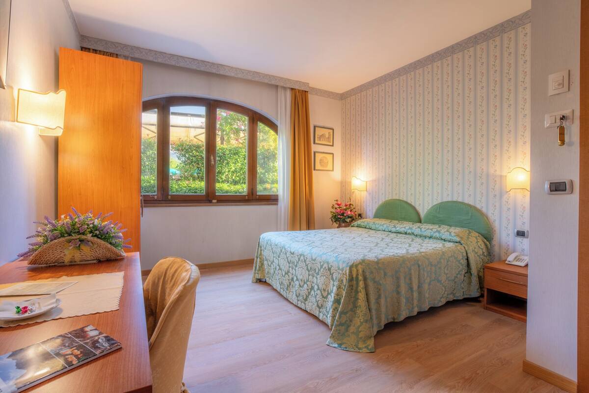 A bedroom with a bed, a desk, a chair, a window, and a door.