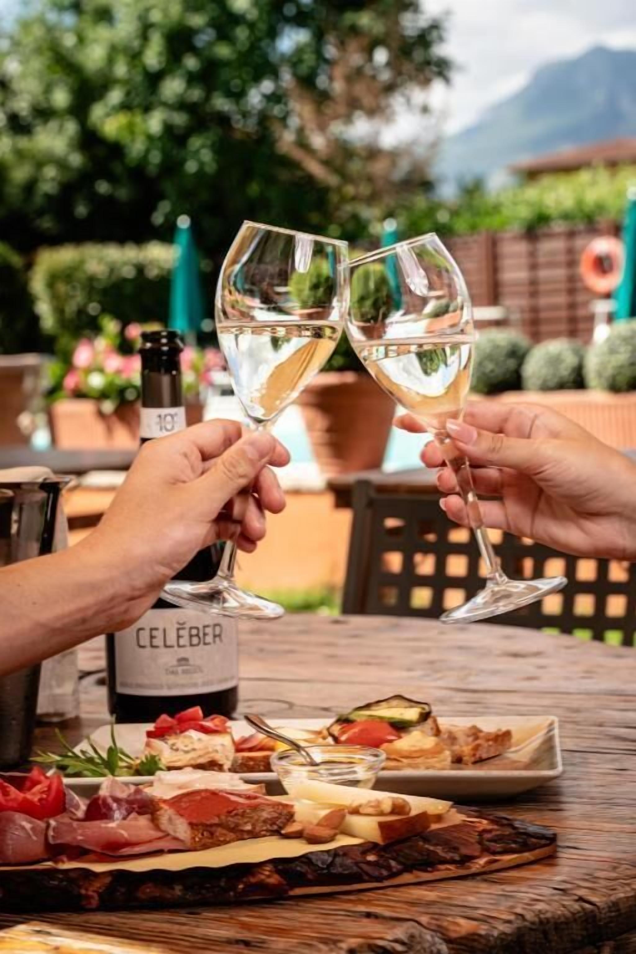 Two people toasting with wine glasses, a bottle of Celeser wine, and a variety of appetizers on a wooden table.