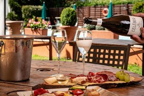 A bottle of CCELEBER wine being poured into two glasses on a wooden table with a variety of cheeses, meats, and grapes. - Hotel Ristorante La Lanterna (Castelnuovo di Garfagnana)