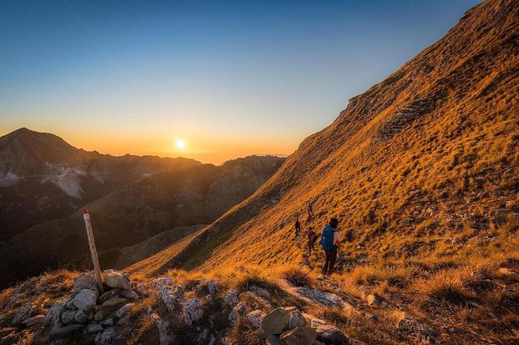 A hiker on a mountain trail with a sunrise in the background.