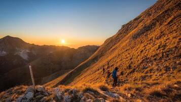 A hiker on a mountain trail with a sunrise in the background.