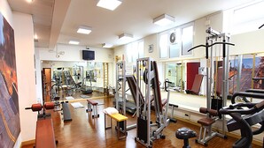 Ein Fitnessraum mit unterschiedlichen Trainingsgeräten, einer Bank und einer Spiegelwand.