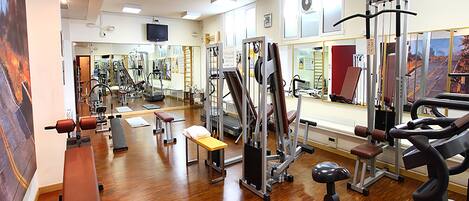 Un gimnasio con equipo de ejercicio diverso, una banca y un muro con espejos.