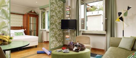 Une chambre d’hôtel comprenant un lit, un canapé, une télévision, un bureau avec une lampe et une fenêtre avec des rideaux.