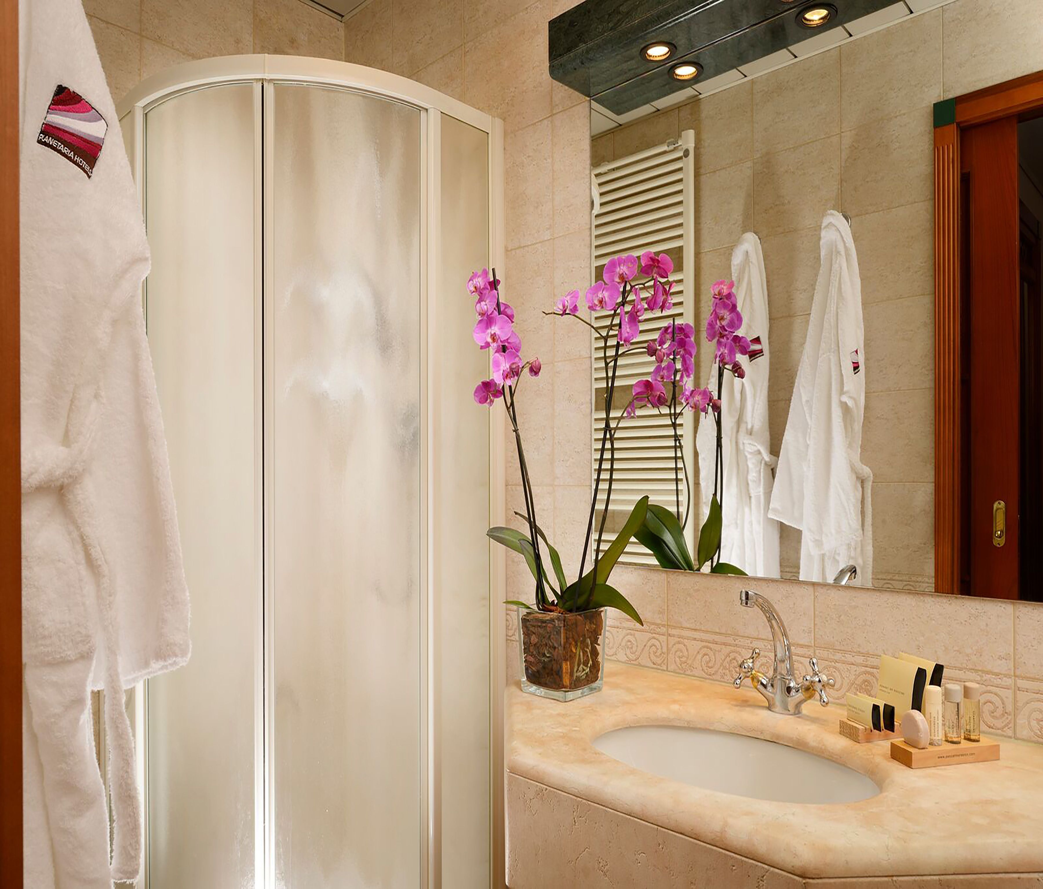 Une salle de bain avec une baignoire blanche, un lavabo avec des articles de toilette et des orchidées roses.