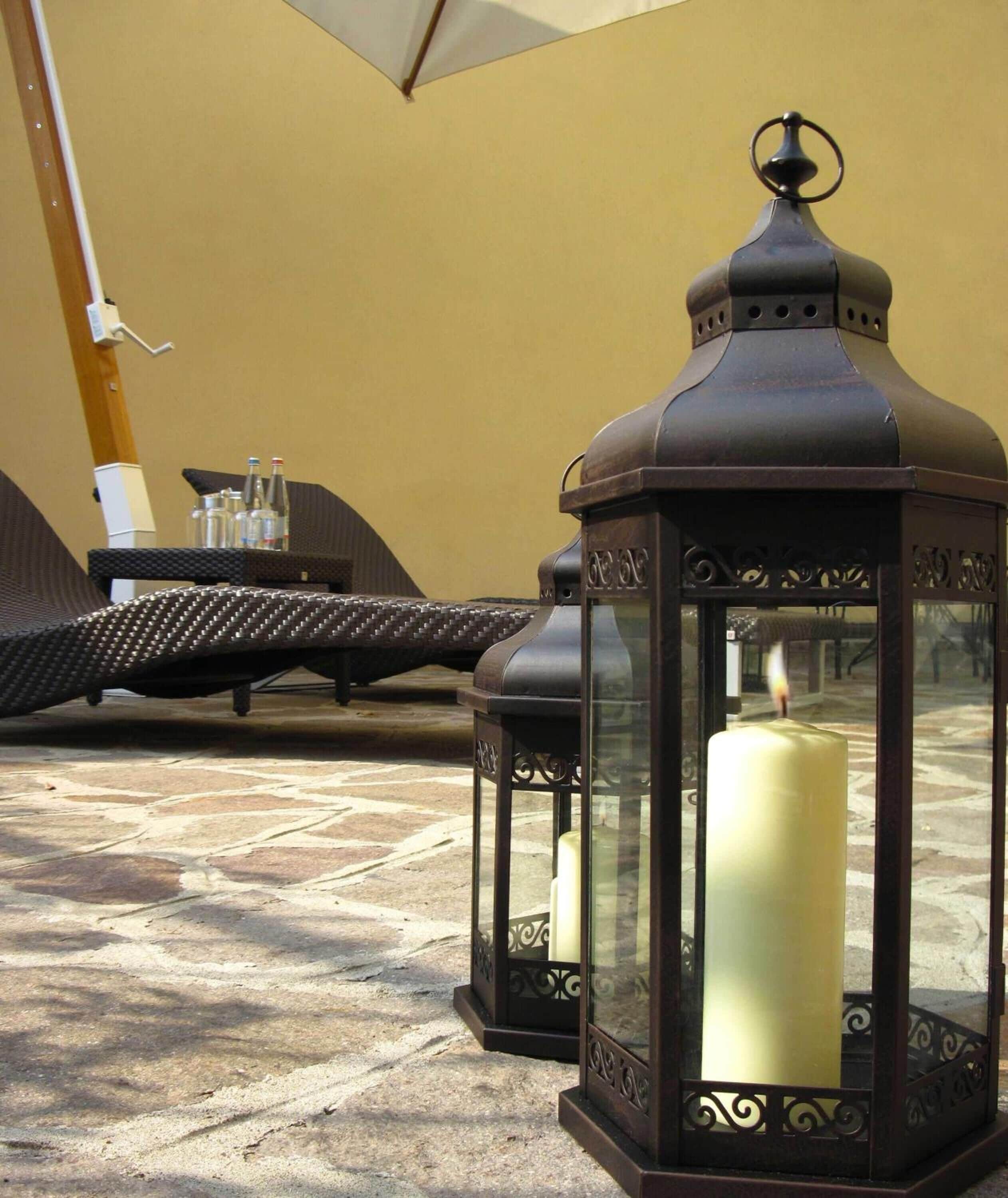 Two black lanterns with candles, a table with bottles, and a chair.