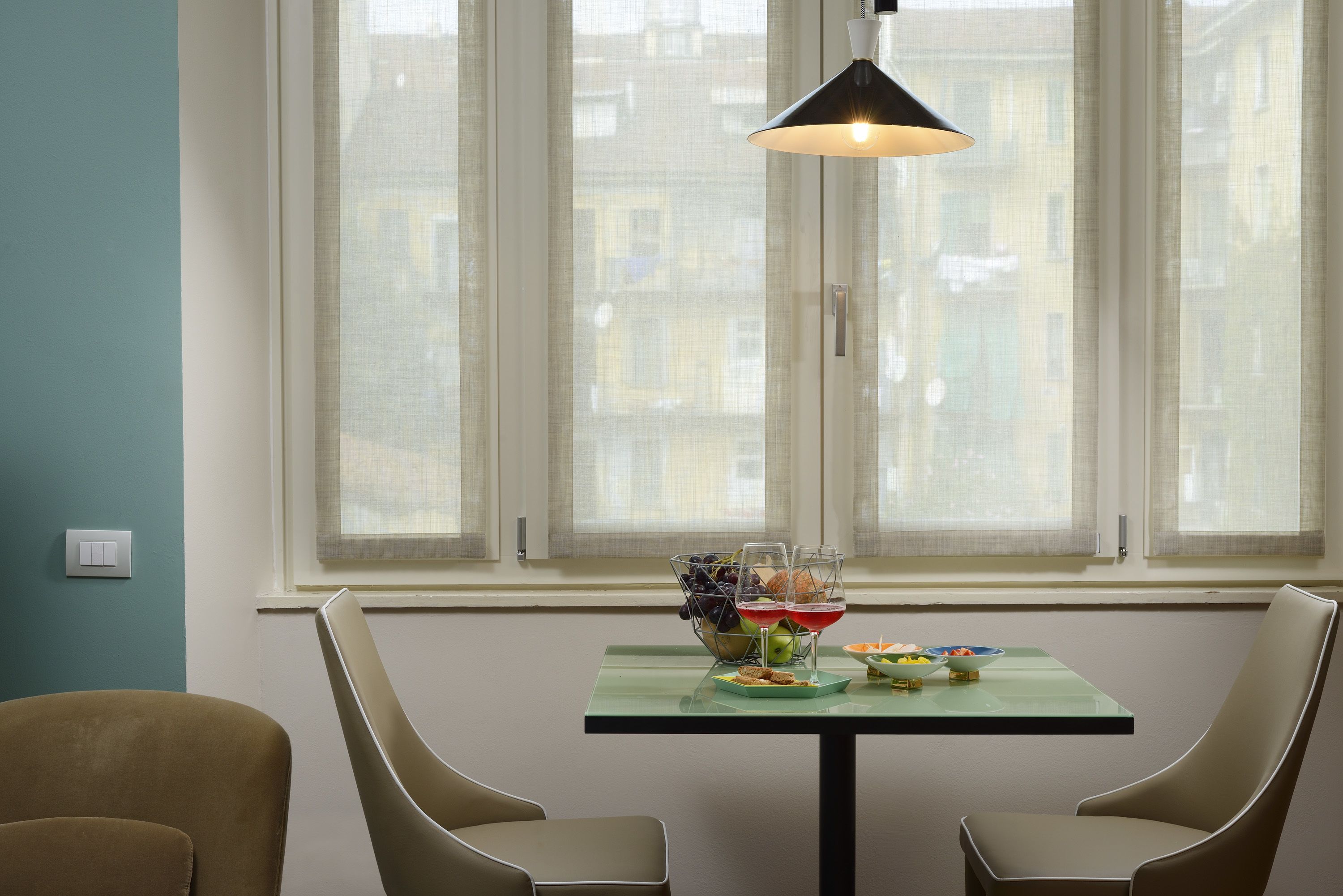 A dining area with a table set for two, a bowl of fruit, and two glasses of red wine.
